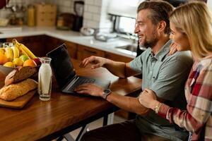 Cheerful couple enjoys a light-hearted moment in their sunny kitchen, working on laptop surrounded by a healthy breakfast photo