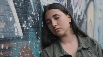 portrait of a young sad brunette hipster girl with long hair near the wall with graffiti video