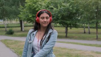 beautiful cheerful happy girl in denim clothes dancing in the park during the day listening to music with headphones. Fun mood video