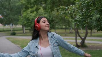 bellissimo allegro ragazza nel rosso cuffie passeggiate giù il strada nel soleggiato tempo metereologico e balli ascoltando per musica. video