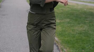 A young brunette girl in a good mood in white sneakers and khaki clothes dancing in the park to the music while holding a portable speaker in her hand. video