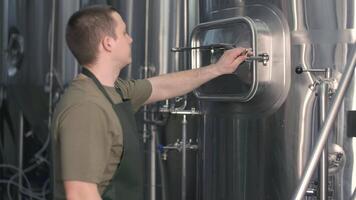 A young male brewer pulls spent malt from a beer tank for brewing beer. Beer production video