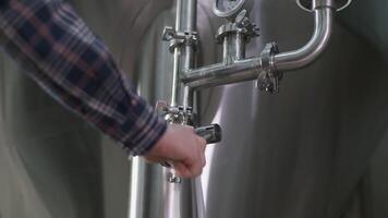 A male brewer opens a tap for brewing beer from a beer tank to a keg. Close-up 4K video