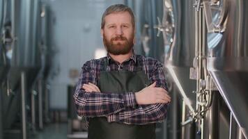 retrato de un empresario cervecero brutal hombre con un barba mirando a el cámara y sonriente mientras en pie en un cerveza fábrica video