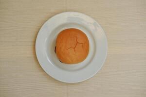 Hamburger bun on a white plate on a wooden table. photo