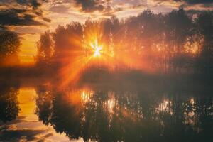 amanecer en un lago o río con un cielo reflejado en el agua, abedul arboles en el apuntalar y el rayos de sol rotura mediante ellos y niebla en otoño. estética de Clásico película. foto