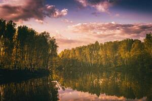 amanecer o puesta de sol en un lago o río con nublado cielo reflexión en el agua en Hora de verano. estética de Clásico película. foto