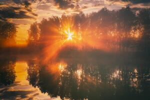 amanecer en un lago o río con un cielo reflejado en el agua, abedul arboles en el apuntalar y el rayos de sol rotura mediante ellos y niebla en otoño. estética de Clásico película. foto