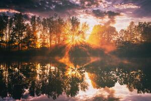 amanecer en un lago o río con un cielo reflejado en el agua, abedul arboles en el apuntalar y el rayos de sol rotura mediante ellos y niebla en otoño. estética de Clásico película. foto