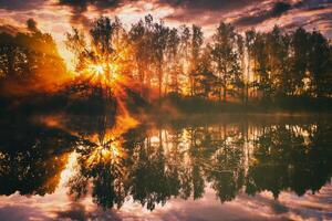 amanecer en un lago o río con un cielo reflejado en el agua, abedul arboles en el apuntalar y el rayos de sol rotura mediante ellos y niebla en otoño. estética de Clásico película. foto