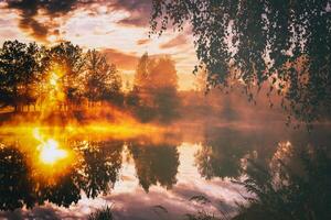 Dawn on a lake or river with a sky reflected in the water, birch trees on the shore and the sunbeams breaking through them and fog in autumn. Aesthetics of vintage film. photo