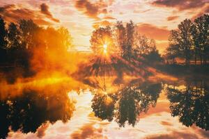 amanecer en un lago o río con un cielo reflejado en el agua, abedul arboles en el apuntalar y el rayos de sol rotura mediante ellos y niebla en otoño. estética de Clásico película. foto