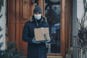 hogar entrega compras caja hombre vistiendo guantes y protector máscara entregando paquetes a puerta. foto