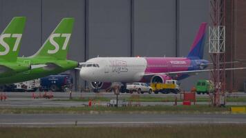 NOVOSIBIRSK, RUSSIAN FEDERATION - JUNE 10, 2020. Airbus A321, HA-LVB of Wizz Air taxiing at Tolmachevo airport. Row of S7 Airlines aircraft parked at the terminal video