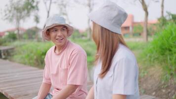 A man sits on a bridge by a river pond with a woman in love talking in a bright morning during a romantic atmosphere. Seasonal concept, Valentine's Day. video