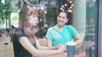 Lanza libre joven mujer chateando acerca de trabajo y sentado a mesa con ordenador portátil en ciudad cafetería, mirando mediante ventana, chateando con sonrisas y mano gestos utilizar computadora video