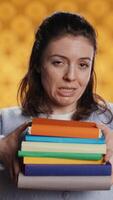 Vertical Woman choosing between physical books and ebooks, favoring ereader for lightness, studio background. Bookworm picking digital literature on tablet in front of heavy stack of novels, camera B video