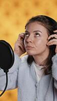 Vertical Woman with headset on starting job, narrating book word for word to produce audiobook. Narrator putting headphones on, using mic to produce digital recording of novel, studio background, camera A video