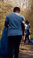 Diverse activists group using claw tools to grab trash and plastic, storing it in garbage disposal bags. People gathering to collect rubbish and recycling for sustainable lifestyle. Camera B. video