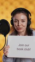 Vertical Joyous woman filming promotional for world book day using microphone, studio background. Happy content creator promoting reading, gaining awareness for literature importance, camera B video