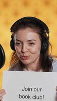 Vertical Joyous woman filming promotional for world book day using microphone, studio background. Happy content creator promoting reading, gaining awareness for literature importance, camera A video