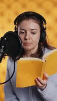 Vertical Woman does voiceover reading of book to produce audiobook using dramatic acting. Narrator uses storytelling skills and expressive sounds while producing recording of novel, studio background, camera B video