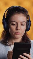 vertikal kvinna bär hörlurar, praktiserande ny språk ordförråd använder sig av uppkopplad app på läsplatta, isolerat över studio bakgrund. lady tala utländsk fraser, läsning dem på enhet skärm video