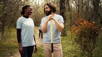 Portrait of two activists clearing up the forest surroundings by collecting garbage, growing new trees and picking up trash. Eco friendly enthusiasts preserving environments and wildlife. Camera B. video