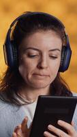 Vertical Woman wearing headphones, practicing new language using internet app on digital tablet, isolated over studio background. Person repeating foreign words, reading them on device video