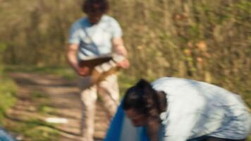 vielfältig Freiwillige Sammeln Müll und Müll von das Wald Bereich, Kampf Umwelt Verschmutzung und Erhaltung. Gruppe von Aktivisten Reinigung oben das Wald, Recycling Plastik Abfall. Kamera a. video