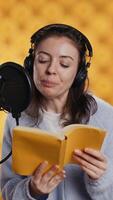 Vertical Narrator wearing headphones, reading aloud from book into microphone, exhaling after finally finishing job. Person recording audiobook, creating engaging media content for listeners, camera B video