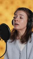 Vertical Voice actor reading book, recording for audiobook production using microphone and headset, studio background. Person using mic and headphones to produce digital recording of novel, camera A video