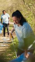 miljö- aktivist plockning upp skräp med en klo verktyg och återvinning, skyddande de naturlig skog livsmiljö och håller på med skräp städa. kvinna håller på med frivillig arbete till sluta förorening. kamera a. video