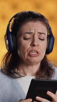 Vertical Voice actor frowns while reading ebook, portraying character, studio background. Woman reenacting digital recording of novel, interpreting furious antagonist, reading text from tablet, camera A video