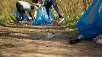 People picking up trash and plastic bottles from the forest area, protecting the natural environment and doing voluntary work. Activists group cleaning the woods, recycling waste. Camera A. video