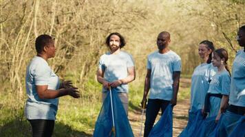 vielfältig Gruppe von Freiwillige Kampf Wald Verschmutzung durch Sammeln Müll im Müll Taschen, pflücken oben Müll und Müll. Aktivisten Arbeiten auf konservieren natürlich Lebensraum, Verantwortung. Kamera a. video