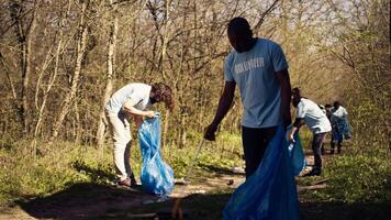 africano americano uomo volontario raccolta spazzatura e plastica rifiuto con pinza, afferrando sciocchezze e raccolta differenziata nel un' spazzatura disposizione. attivista la lotta contro foresta inquinamento e illegale dumping. telecamera b. video