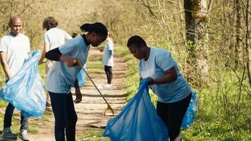 ambientale attivisti raccolta sciocchezze e plastica rifiuto nel spazzatura Borsa, utilizzando più piccolo pulire utensili per raccogliere su spazzatura a partire dal il foresta. donne fare volontario opera per proteggere ecosistema. telecamera un. video