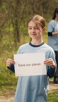 retrato de dulce niña con salvar nuestra planeta póster en contra contaminación y ilegal dumping, trabajar como voluntario a restaurar y preservar naturaleza en el bosque. pequeño niño muestra conciencia signo. cámara una. video