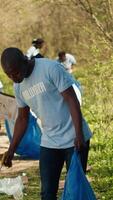 africano americano hombre voluntario coleccionar basura y el plastico residuos con tenazas, agarrando basura y reciclaje en un basura desecho. activista combatiendo bosque contaminación y ilegal dumping. cámara una. video