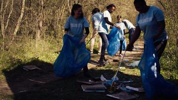 Group of diverse volunteers collecting rubbish from the woods and recycling in a garbage disposal bag, litter cleanup responsibility. Ecology activists picking up trash and plastic waste. Camera B. video