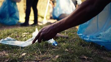 People supporting cleanup of the natural environment by grabbing recyclables and trash objects from the woods, collecting in a garbage bag. Using utensils to pick up rubbish. Close up. Camera B. video