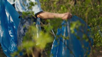 diverso grupo de voluntarios cosecha arriba basura y el plastico a reciclar, trabajando juntos a preservar y restaurar naturaleza. activistas combatiendo ilegal dumping, coleccionar basura en bolsas. cámara una. video