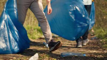 Diverse activists cleaning up rubbish in a garbage disposal bag, environmental conservation concept. Volunteers protecting the forest ecosystem, collecting rubbish with claw tool. Camera A. video