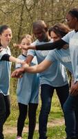 Cheerful proud team of activists join forces to clean a forest, celebrating their volunteering work by connecting hands together. Happy people showing responsibility for the environment. Camera A. video