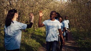 Activists congratulating each other with a high five after a successful teamwork, showing perseverance in collecting rubbish and plastic waste from forest environment. A job well done. Camera B. video