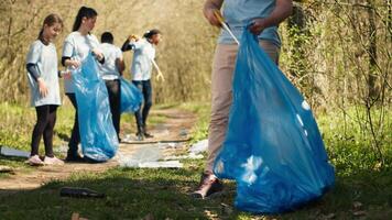 man aktivist använder sig av tång till hugg sopor och plast avfall, plockning upp skräp och rengöring de skog område. volontär- sortering skräp och återvinning Det, bevara de natur. kamera a. video