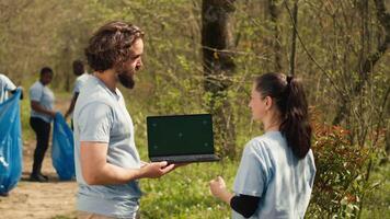 Mannschaft von Klima und Natur Aktivisten mit Laptop mit grüner Bildschirm in der Nähe von ein Wald, Freiwilligenarbeit zu wählen oben Müll und Pflanze Bäume zum Zukunft Generationen. Umwelt Schutz. Kamera a. video