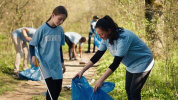 mam en kind verzamelen onzin van de Woud Oppervlakte gebruik makend van een lang klauw gereedschap en vuilnis verwijdering Tassen. weinig meisje plukken omhoog uitschot en plastic verspilling met haar moeder, ecologisch gerechtigheid. camera a. video