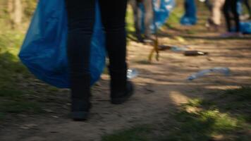 Diverse activists group using claw tools to grab trash and plastic, storing it in garbage disposal bags. People gathering to collect rubbish and recycling for sustainable lifestyle. Camera A. video